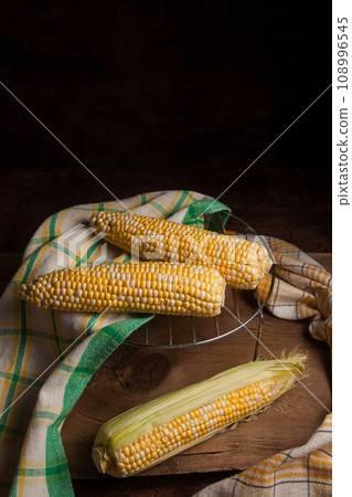 Several cobs sweet corn with green leaves on wooden background.. Several cobs sweet corn with green leaves on wooden background.. 108996545