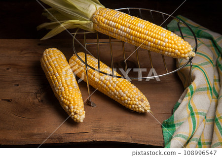 Several cobs sweet corn with green leaves on wooden background.. Several cobs sweet corn with green leaves on wooden background.. 108996547