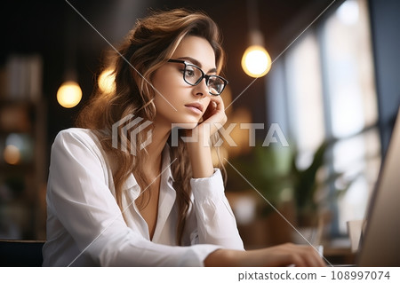 Bored young woman dressed in shirt sitting at her workplace at the office, looking at computer Bored young woman dressed in shirt sitting at her workplace at the office, looking at computer 108997074