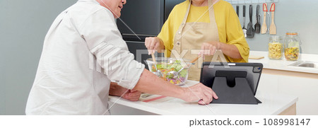 Asian senior couple watching recipe with tablet making salad vegetable together in the kitchen. 108998147