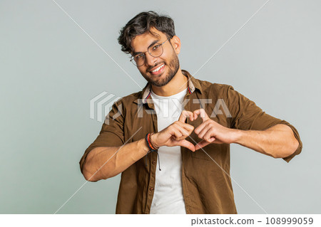 Smiling handsome man makes heart gesture demonstrates love sign expresses good feelings and sympathy Smiling handsome man makes heart gesture demonstrates love sign expresses good feelings and sympathy 108999059