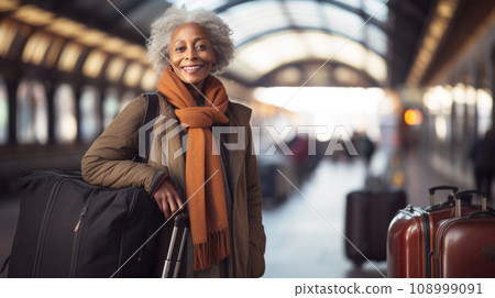 A radiant senior woman with a joyous smile prepares for her next adventure at the train station, her eyes alight with the excitement of travel at the bustling train platform 108999091