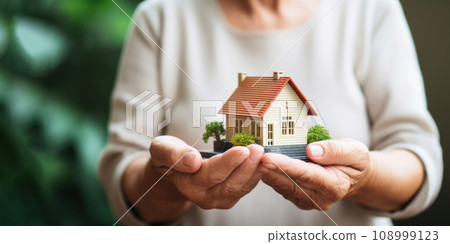 Hands of elderly person holding miniature house, symbolizing cherished value of home and the dream of secure, affordable housing for all, representing hope and importance of stability in later life Hands of elderly person holding miniature house, symbolizing cherished value of home and the dream of secure, affordable housing for all, representing hope and importance of stability in later life 108999123