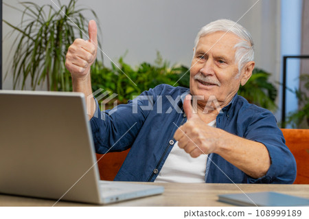 Senior grandfather man at home looking at camera making video conference call with friends family Senior grandfather man at home looking at camera making video conference call with friends family 108999189
