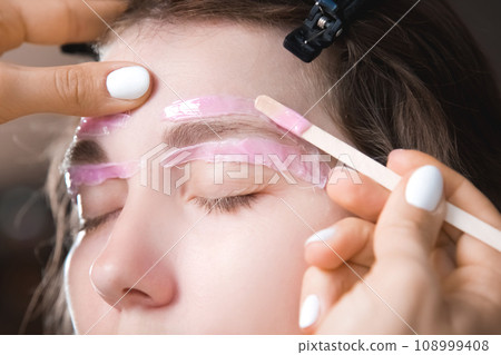 Hair removal, beauty and health concept. A young girl is getting an epilation procedure. A processional beauty worker is making depilation with hot wax 108999408