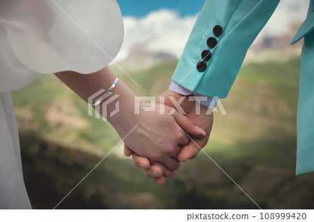 Touching hands of a man and a woman, close-up. Strong tender embrace of two lovers against the backdrop of the mountains. The hands of a young couple hold each other. Feeling of love 108999420