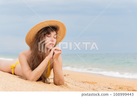 Summer lifestyle. Portrait of a beautiful girl with a slim body in a bikini enjoying life and lying with her eyes closed on the sand on the beach of a tropical island. Vacation Summer lifestyle. Portrait of a beautiful girl with a slim body in a bikini enjoying life and lying with her eyes closed on the sand on the beach of a tropical island. Vacation 108999443