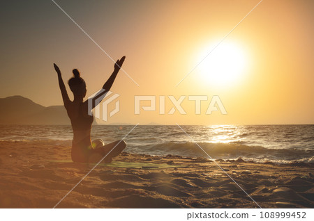 gorgeous woman practicing yoga, raising her arms, feeling so good and happy, young woman seeking enlightenment through meditation on the sea 108999452
