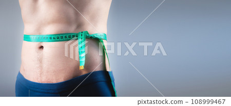 Close-up of an athlete measuring body fat with a centimeter on a gray background. A man lost weight thanks to a diet and pumped up his abs, photo for banner Close-up of an athlete measuring body fat with a centimeter on a gray background. A man lost weight thanks to a diet and pumped up his abs, photo for banner 108999467