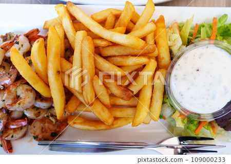Delicious serving of French fries, fried shrimps, and garlic sauce on a pristine white plate 109000233