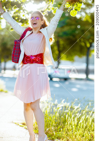 Full length portrait of happy woman in dress and jacket in city 109000445