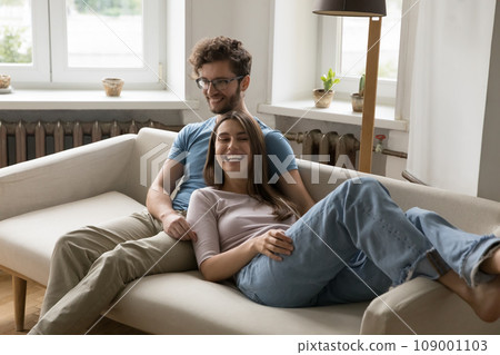 Couple laughing relaxing together on cozy couch in living room 109001103