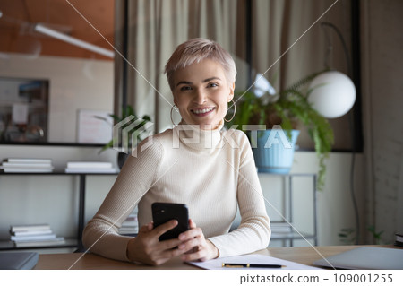 Happy short haired businesswoman with smartphone at office workplace Happy short haired businesswoman with smartphone at office workplace 109001255