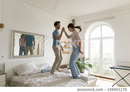 Funny couple jumping on bed in modern bedroom 109001276