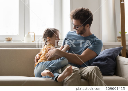 Playful girl tickling father sitting on couch Playful girl tickling father sitting on couch 109001415