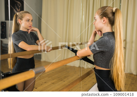 Female ballet dancer resting at barre and mirror in dance studio - dance and ballerina concept Female ballet dancer resting at barre and mirror in dance studio - dance and ballerina concept 109001418