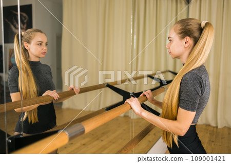 Female ballet dancer resting at barre and mirror in dance studio - dance and ballerina concept 109001421