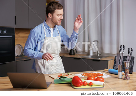 Young handsome man is preparing pizza and salad in the kitchen. The man enjoys the process of cooking. Young handsome man is preparing pizza and salad in the kitchen. The man enjoys the process of cooking. 109001466