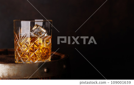 Whiskey glass with ice on a rustic barrel, a classic sip 109001639