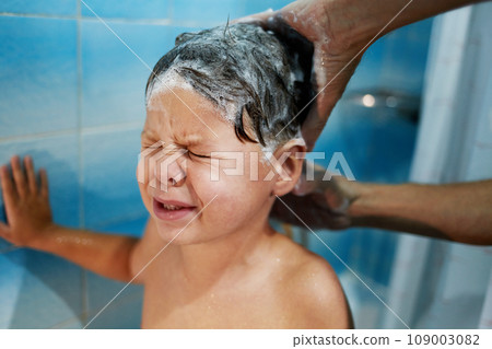 Dad's hands wash the little boy's head in the bathroom. The child does not like to wash his hair and cries. Dad's hands wash the little boy's head in the bathroom. The child does not like to wash his hair and cries. 109003082
