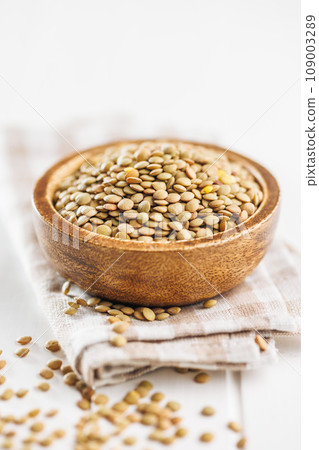 Uncooked lentil legumes in bowl on white table. 109003289