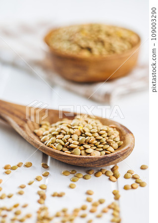 Uncooked lentil legumes in wooden spoon on white table. Uncooked lentil legumes in wooden spoon on white table. 109003290