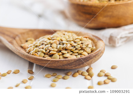 Uncooked lentil legumes in wooden spoon on white table. Uncooked lentil legumes in wooden spoon on white table. 109003291