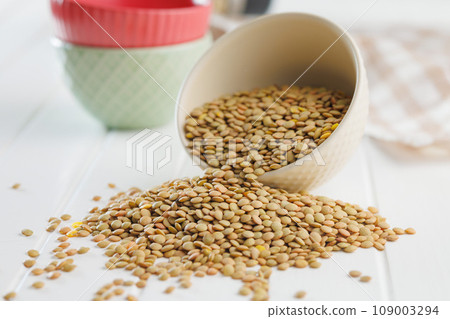 Uncooked lentil legumes in bowl on white table. 109003294