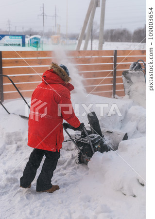 A man clear snow from backyard with snow blower. Winter season and snow blower equipment A man clear snow from backyard with snow blower. Winter season and snow blower equipment 109003654