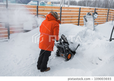 A man clear snow from backyard with snow blower. Winter season and snow blower equipment A man clear snow from backyard with snow blower. Winter season and snow blower equipment 109003693