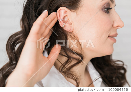 Cropped close-up shot of a young woman with asymmetrical silver ear cuffs. Female with metal ear cuffs, side view 109004556