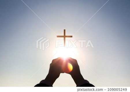 Brightly shining sunlight and silhouette of Christian hands holding high the cross of Jesus Christ symbolizing death and resurrection 109005249