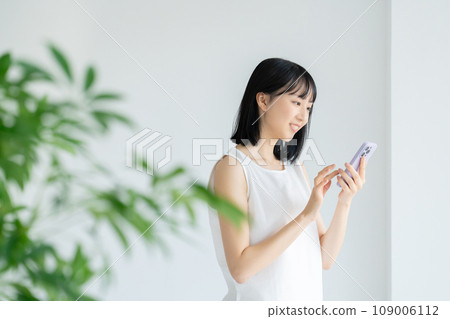 A woman in white clothes using a smartphone 109006112