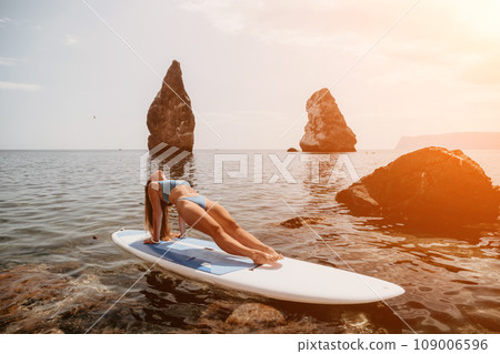 Woman sup yoga. Happy sporty woman practising yoga pilates on paddle sup surfboard. Female stretching doing workout on sea water. Modern individual female hipster outdoor summer sport activity. Woman sup yoga. Happy sporty woman practising yoga pilates on paddle sup surfboard. Female stretching doing workout on sea water. Modern individual female hipster outdoor summer sport activity. 109006596