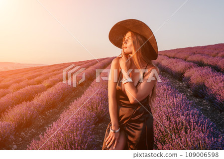 Woman lavender field. Happy carefree woman in black dress and hat with large brim walking in a lavender field during sunset. Perfect for inspirational and warm concepts in travel and wanderlust. Woman lavender field. Happy carefree woman in black dress and hat with large brim walking in a lavender field during sunset. Perfect for inspirational and warm concepts in travel and wanderlust. 109006598
