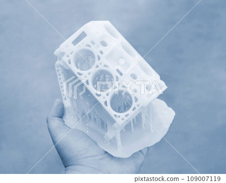 Person holding in palm of hand prototype of car engine printed on 3D printer from molten white plastic. Three-dimensional model. Additive progressive modeling technology. Modern new printing industry. 109007119