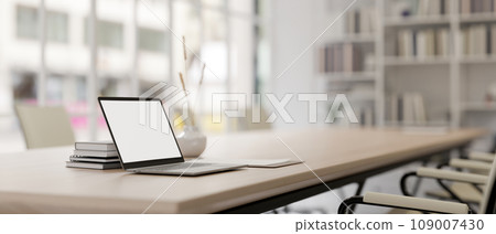 A white-screen laptop mockup on a meeting table in a modern meeting room. 109007430