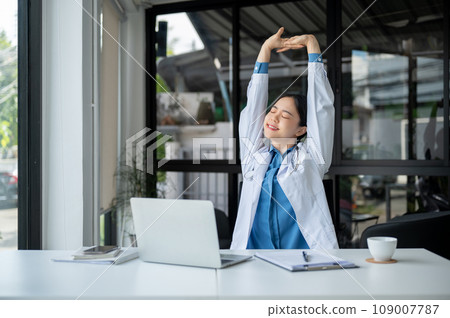 A relaxed Asian female doctor is stretching her arms and taking a break after work at her desk. A relaxed Asian female doctor is stretching her arms and taking a break after work at her desk. 109007787