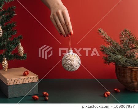 Hand with Christmas ball over table with gift and Christmas trees 109007957