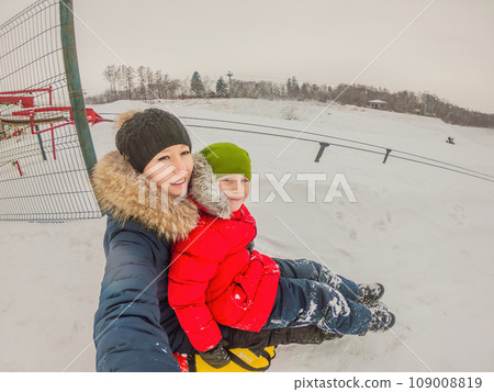A joyous winter scene: mom and son ride together on an inflatable sled, tubing down snowy slopes. Family fun abounds in this delightful winter adventure 109008819