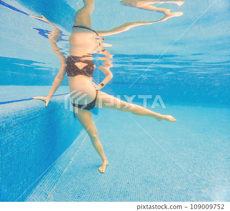 Embracing aquatic fitness, a pregnant woman demonstrates strength and serenity in underwater aerobics, creating a serene and empowering image in the pool 109009752