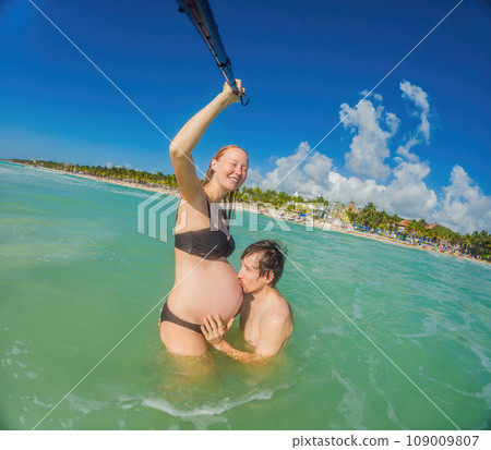 Amidst the tranquil turquoise sea, a pregnant woman and her husband share a serene moment, celebrating the beauty of impending parenthood in the gentle waves 109009807