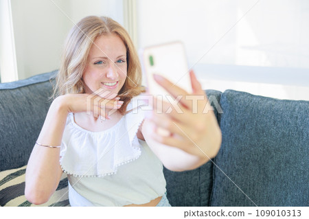 Caucasian girl sitting on the sofa and taking a selfie 109010313