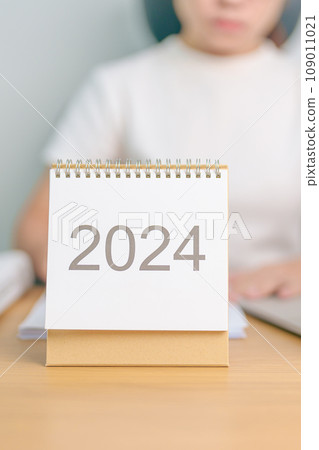 2024 Year Calendar on table with business woman using laptop computer. countdown, Happy New Year, Resolution, Goals, Plan,  Action, Mission and financial Concept 109011021