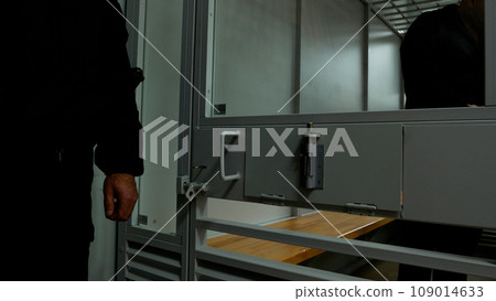 A policeman stands near a cage with a criminal in the courtroom. There is a prisoner in the cage. The work of the court. A policeman stands near a cage with a criminal in the courtroom. There is a prisoner in the cage. The work of the court. 109014633