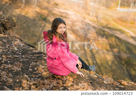 Beautiful happy smiling girl with long hair wearing pink jacket posing in autumn park. Outdoor portrait day light. Autumn mood concept. Generation Z and gen z youth. Copy empty space for text. Beautiful happy smiling girl with long hair wearing pink jacket posing in autumn park. Outdoor portrait day light. Autumn mood concept. Generation Z and gen z youth. Copy empty space for text. 109014723
