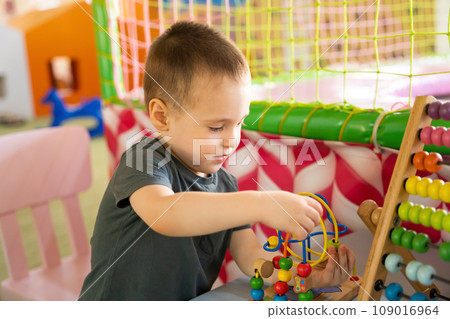 Toddler boy plays with educational wooden toy in children's playroom. Toddler boy plays with educational wooden toy in children's playroom. 109016964