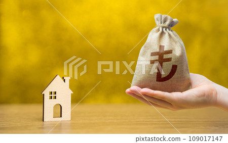 Turkish lira money bag and miniature wooden house on a yellow background. Real estate and affordable housing concept. Mortgage, loan and insurance of apartments. Selling and buying home. 109017147