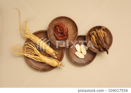 Top view of rare herbal displayed on wooden dishes - ginseng roots, ganoderma mushrooms and red ginseng. Beige background for advertising product and space for design 109017936