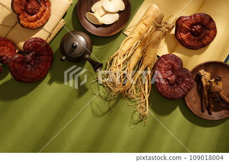 Photo for medicine advertising. Some rare herbs decorated, fresh ginseng roots, red ginseng roots and ganoderma mushrooms displayed on green background. Blank space for presentation product 109018004